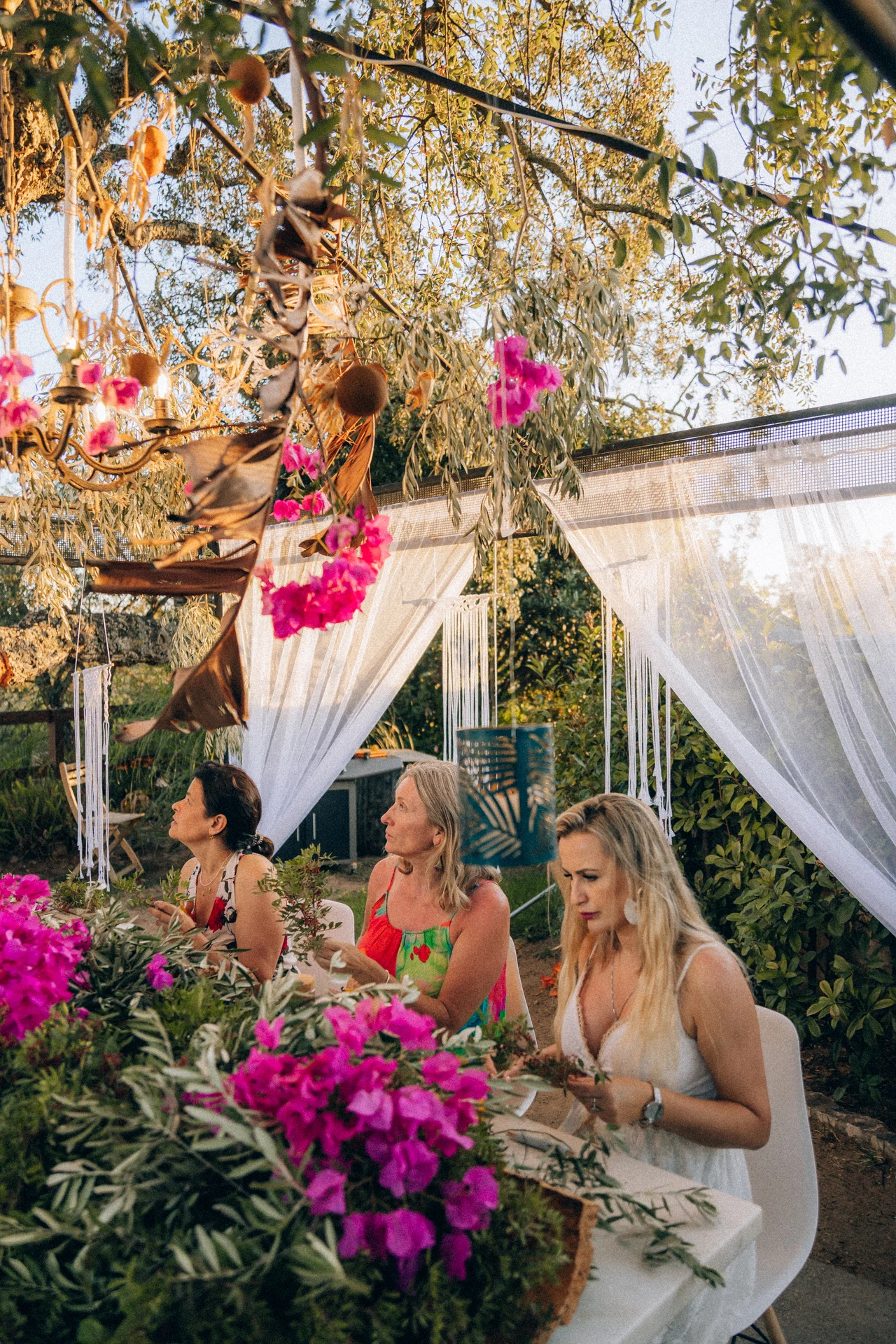 Polka organizuje "babskie wyjazdy" do Portugalii. "Chcę pokazać kobietom, co to spokój" Trzy kobiety siedzą przy elegancko udekorowanym stole na zewnątrz, otoczone zielenią, różowymi kwiatami i białymi zasłonami, które nadają otoczeniu romantyczny i elegancki charakter.