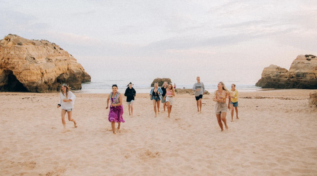Polka organizuje “babskie wyjazdy” do Portugalii Grupa osób biegnących po piaszczystej plaży, w tle widoczne skały i spokojne niebo, atmosfera swobody i radości.