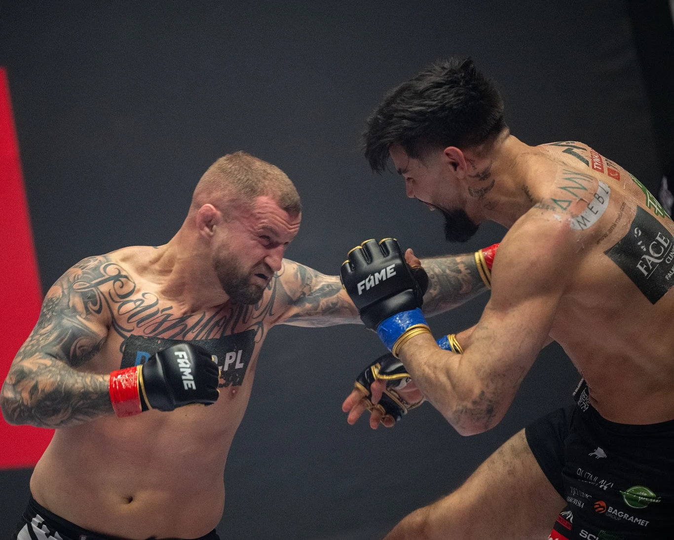 FAME MMA 28: Marcin Wrzosek - Paweł Tyburski Dwóch muskularnych zawodników toczy pojedynek MMA w oktagonie, obaj są w połowie nadzy, prezentują liczne tatuaże, a ich twarze i ciała są napięte w trakcie wymiany ciosów. Intensywność walki podkreślają zacięte miny oraz ściśnięte pięści w rękawicach.