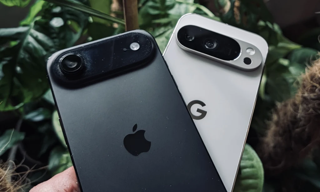 Dwa smartfony, jeden marki Apple z czarną obudową i drugi marki Google z białą obudową, trzymane blisko siebie na tle zielonych liści.