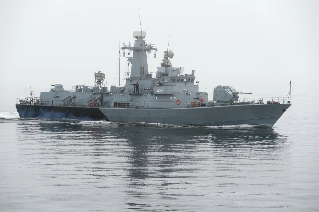 Okręt wojenny płynący po spokojnej wodzie w lekko zamglonej aurze, dobrze widoczne uzbrojenie na pokładzie i nowoczesna infrastruktura okrętu.