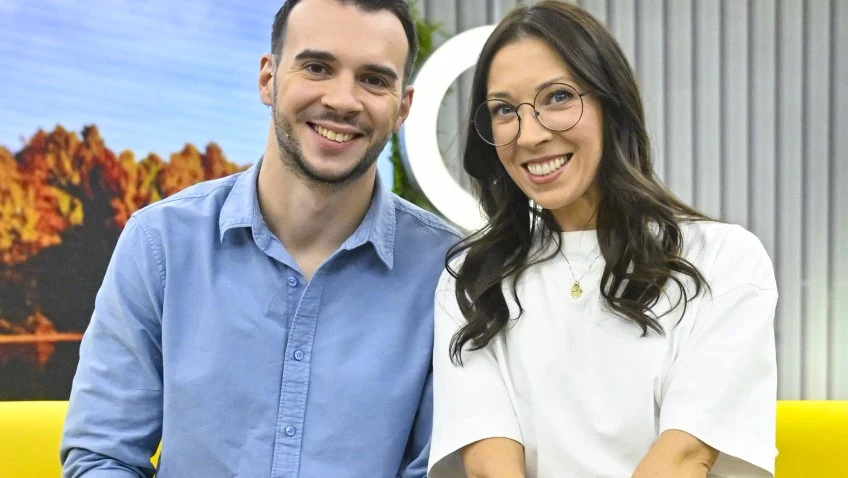 Ada Borek i Albert Kosiński poznali się w "TzG" Dwie uśmiechnięte osoby siedzące na żółtej sofie, mężczyzna w niebieskiej koszuli oraz kobieta w białej bluzce i okularach, w tle widoczna dekoracja z motywem przyrody oraz pionowe panele.