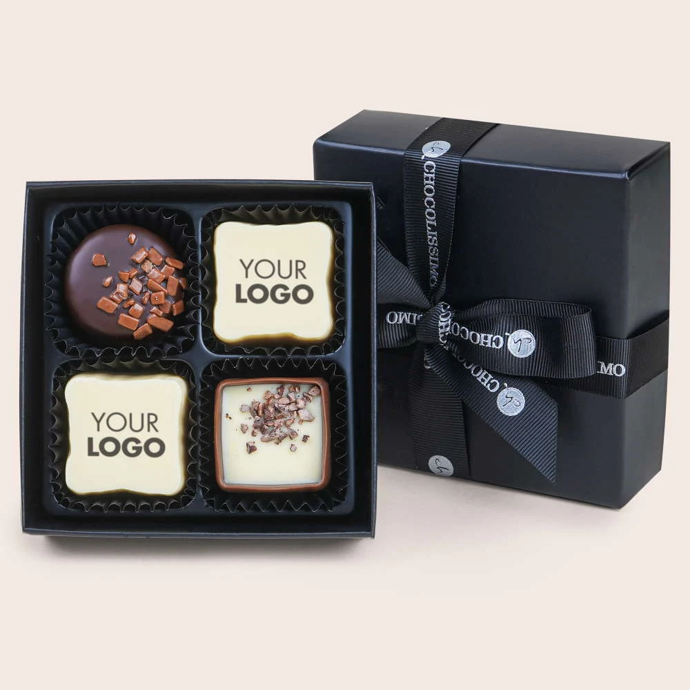 Czarna elegancka pudełko z czterema czekoladkami, z których dwie mają nadruk 'YOUR LOGO', a dwie posypane są kawałkami czekolady. Opakowanie przewiązane ozdobną wstążką.