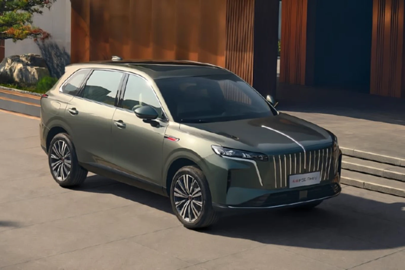 Hongqi HS6 na jednym ładowaniu i tankowaniu przejechał ponad 2300 km Nowoczesny SUV w kolorze zielonym stoi zaparkowany na chodniku przed nowoczesnym budynkiem. Samochód wyróżnia się charakterystycznym dużym grillem z chromowanymi elementami, dużymi reflektorami LED oraz eleganckimi przetłoczeniami na masce. W tle widoc...