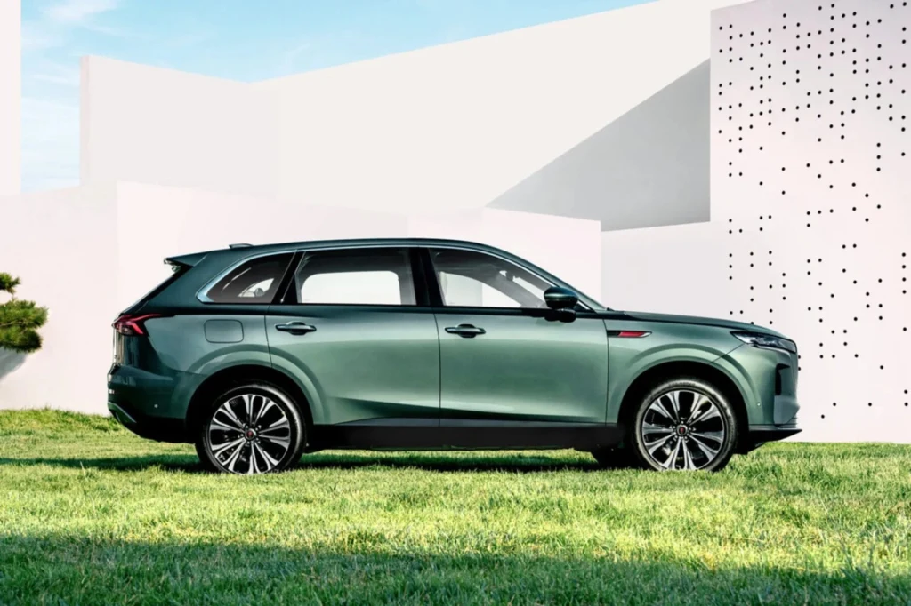 Zielony SUV stoi na trawniku, w tle nowoczesny, biały budynek z geometrycznymi otworami i minimalistyczną architekturą.