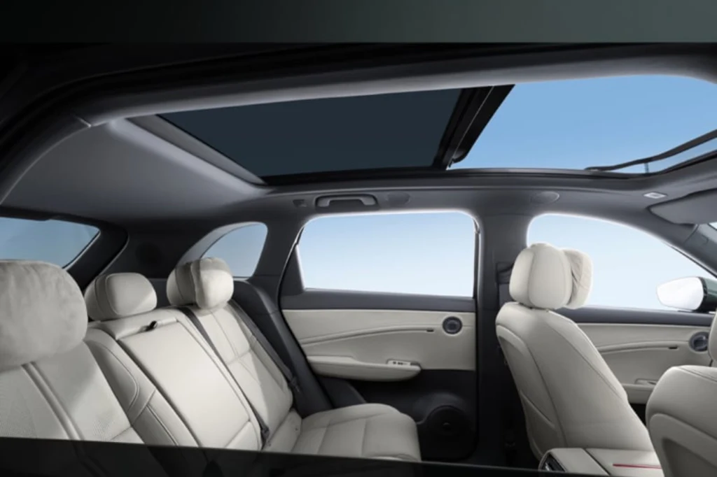 Jasne, skórzane wnętrze samochodu z widocznymi czterema siedzeniami oraz dużym panoramicznym oknem dachowym otwartym na błękitne niebo.