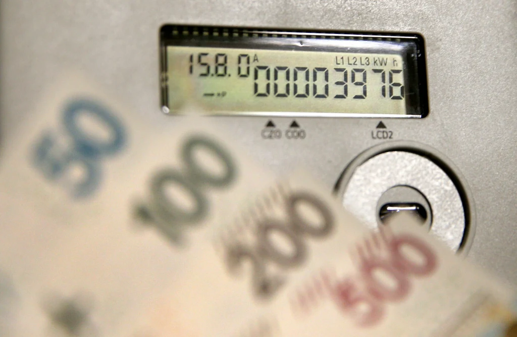 Licznik energii elektrycznej wyświetlający aktualny odczyt, z przodu nieostre polskie banknoty o nominałach 50, 100, 200 i 500 złotych symbolizujące koszty zużycia prądu.