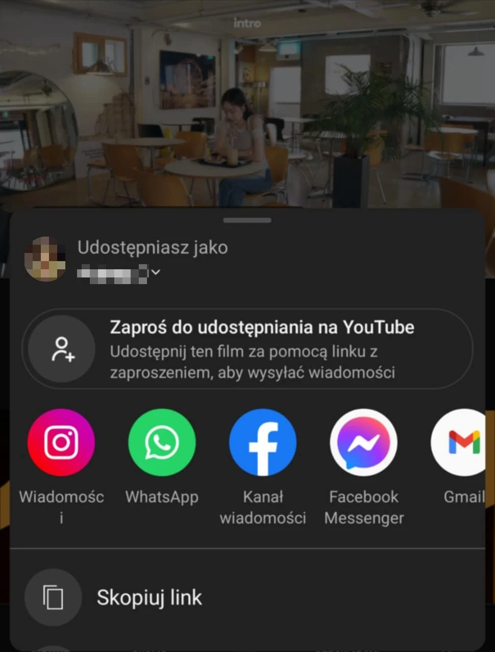 Ekran udostępniania linku z telefonu z widocznymi ikonami aplikacji takich jak Instagram, WhatsApp, Facebook, Facebook Messenger oraz Gmail na tle jasnego, nowoczesnego wnętrza kawiarni lub biura, gdzie przy jednym ze stołów siedzi kobieta z laptopem.