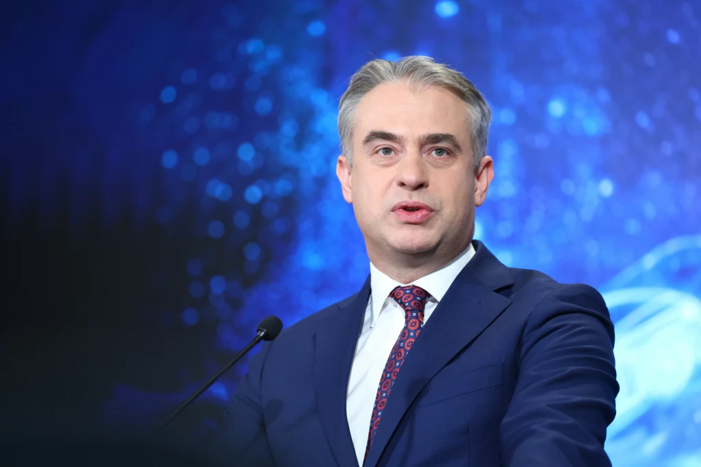 Blokowanie treści w internecie. Sejm przegłosował nowelizację Mężczyzna w garniturze i pod krawatem przemawia do mikrofonu na tle niebieskiego, abstrakcyjnego tła.