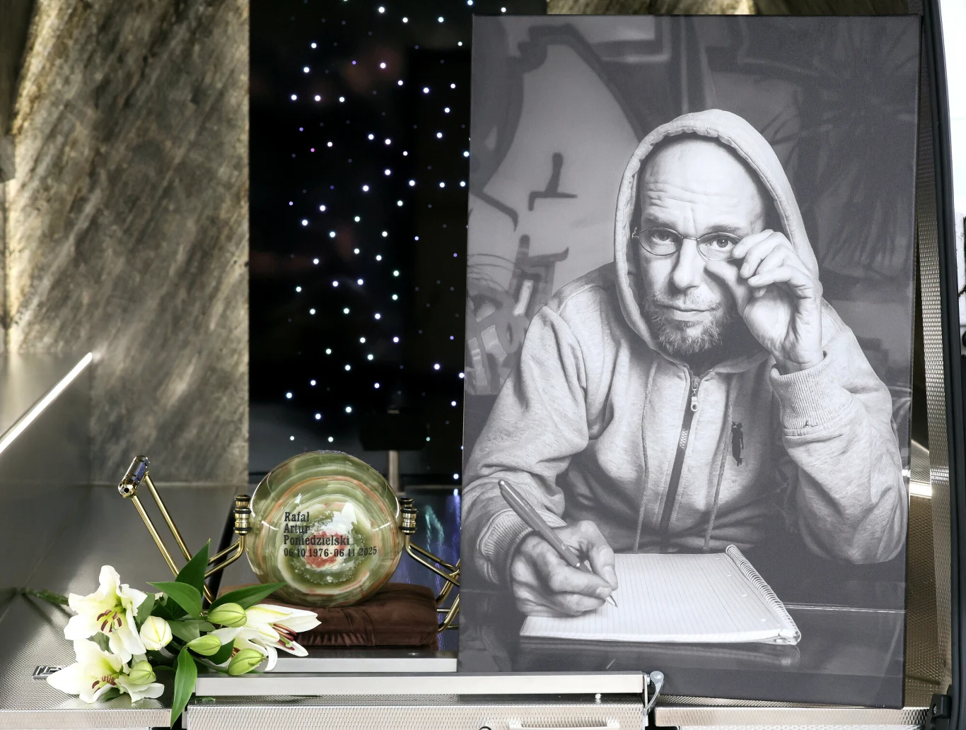 Portret Pono pojawił się na jego grobie Czarno-białe zdjęcie mężczyzny w okularach i bluzie z kapturem spoglądającego przez okulary, z dłonią opartą o notatnik. Obok zdjęcia znajduje się ozdobna kula, bukiet białych lilii oraz czarna płyta z drobinkami świateł.