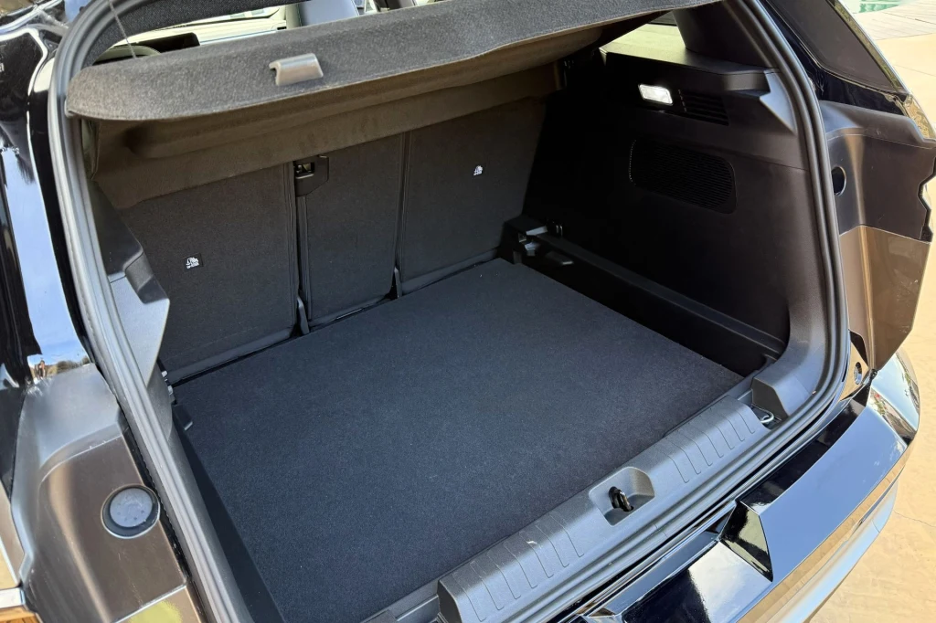 Bagażnik Jeepa Compassa ma 550 litrów. Bagażnik samochodu osobowego z otwartą klapą, duża przestrzeń ładunkowa pokryta czarną wykładziną, podniesiona roleta bagażnika oraz widoczne oparcia tylnych siedzeń.