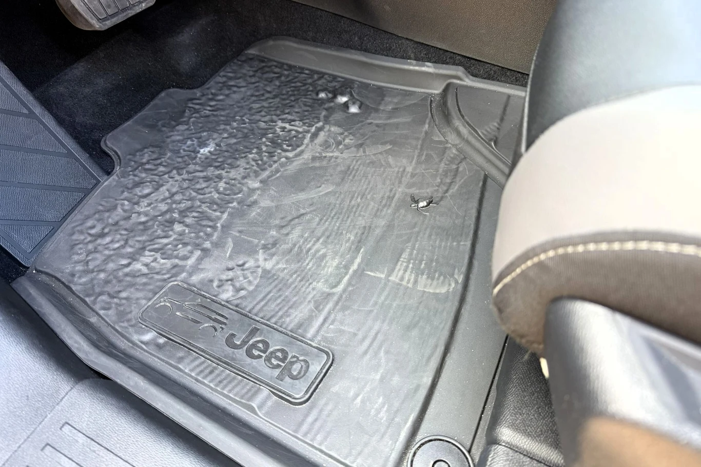 Gumowa mata samochodowa z logo Jeep, o wyraźnie widocznych śladach zużycia i zabrudzenia, ułożona na podłodze pod fotelem pasażera.