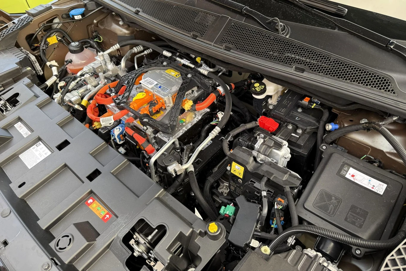 Komora silnika samochodu elektrycznego z widocznymi przewodami wysokiego napięcia oznaczonymi pomarańczowym kolorem oraz licznymi podzespołami elektronicznymi i sterującymi.