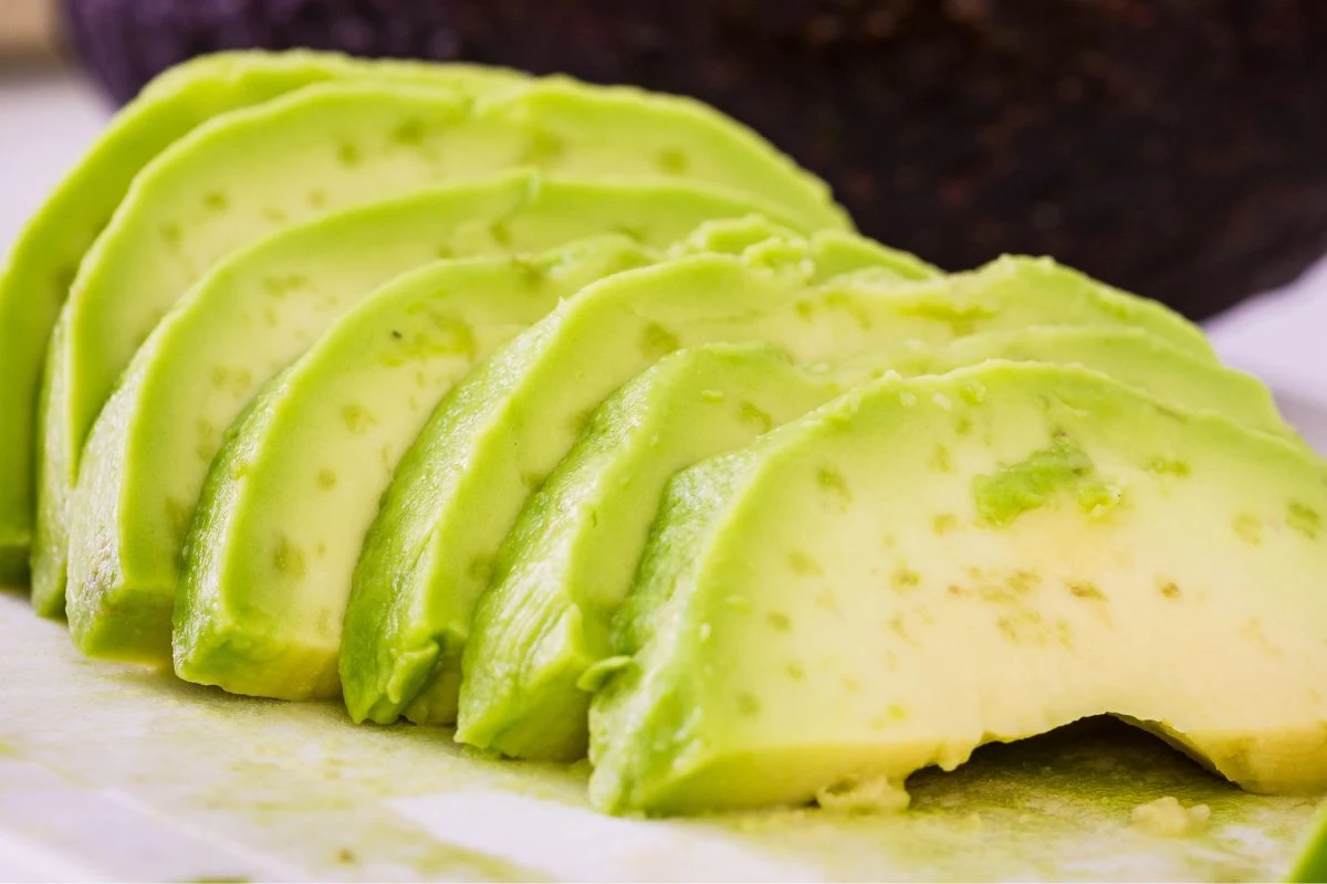 Pokrojone na plasterki dojrzałe awokado o świeżym, kremowym wnętrzu ułożone na jasnej powierzchni.