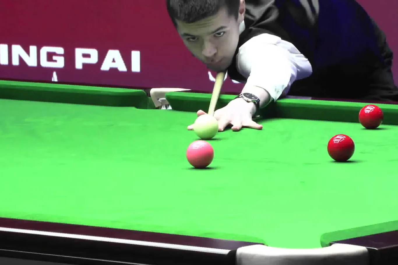 Michał Szubarczyk Mężczyzna w eleganckim stroju pochyla się nad zielonym stołem bilardowym, przygotowując się do uderzenia kijem w białą bilę, wokół której rozmieszczone są czerwone bile.