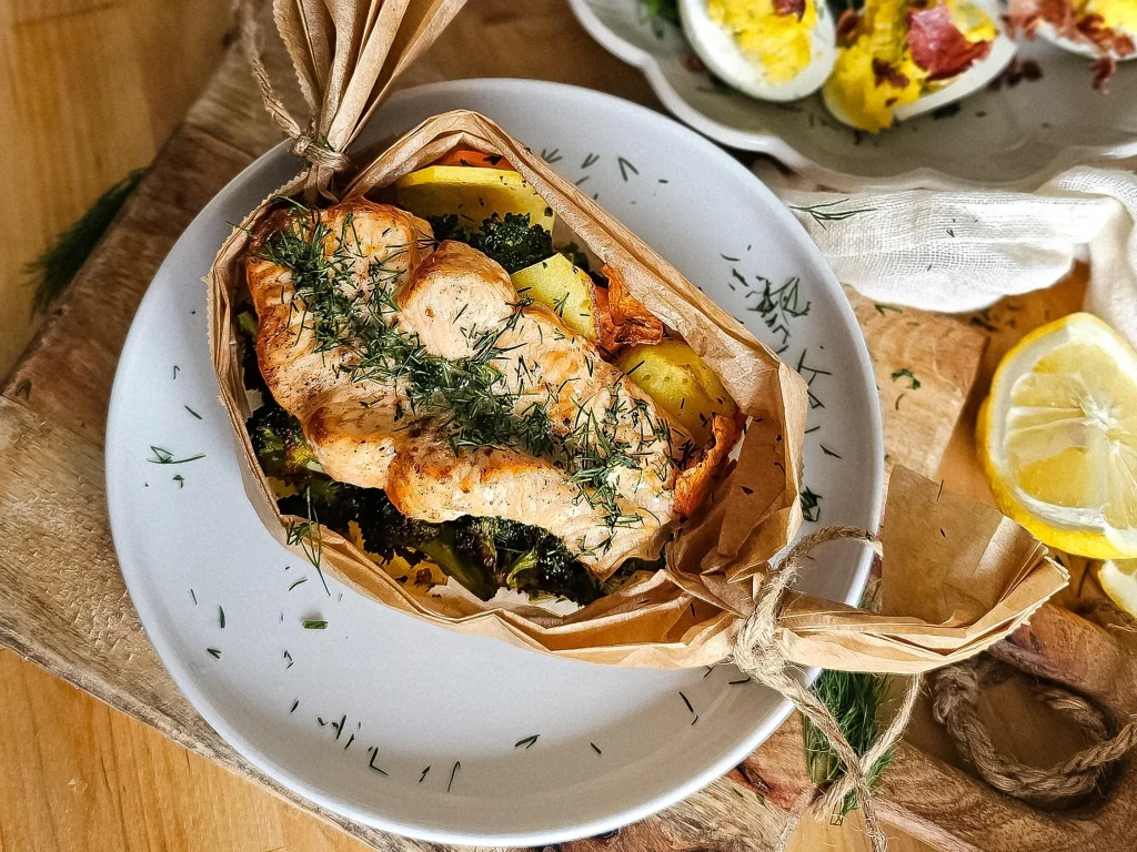 Łososia kroimy na grube steki, nacinamy je pośrodku, doprawiamy sola i pieprzem, układamy na warzywach