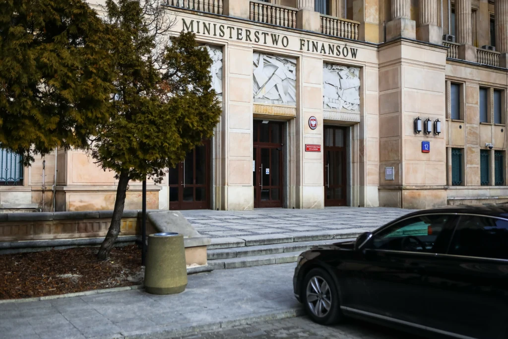 Ministerstwo Finansów po raz pierwszy sprzedało obligacje oparte o wskaźnik POLSTR Gmach Ministerstwa Finansów z widocznym napisem nad wejściem, głównym wejściem z dużymi, szklanymi drzwiami oraz fragmentem zaparkowanego samochodu na pierwszym planie. Po lewej stronie rośnie drzewo, a teren wokół jest uporządkowany, z niewielkimi ele...