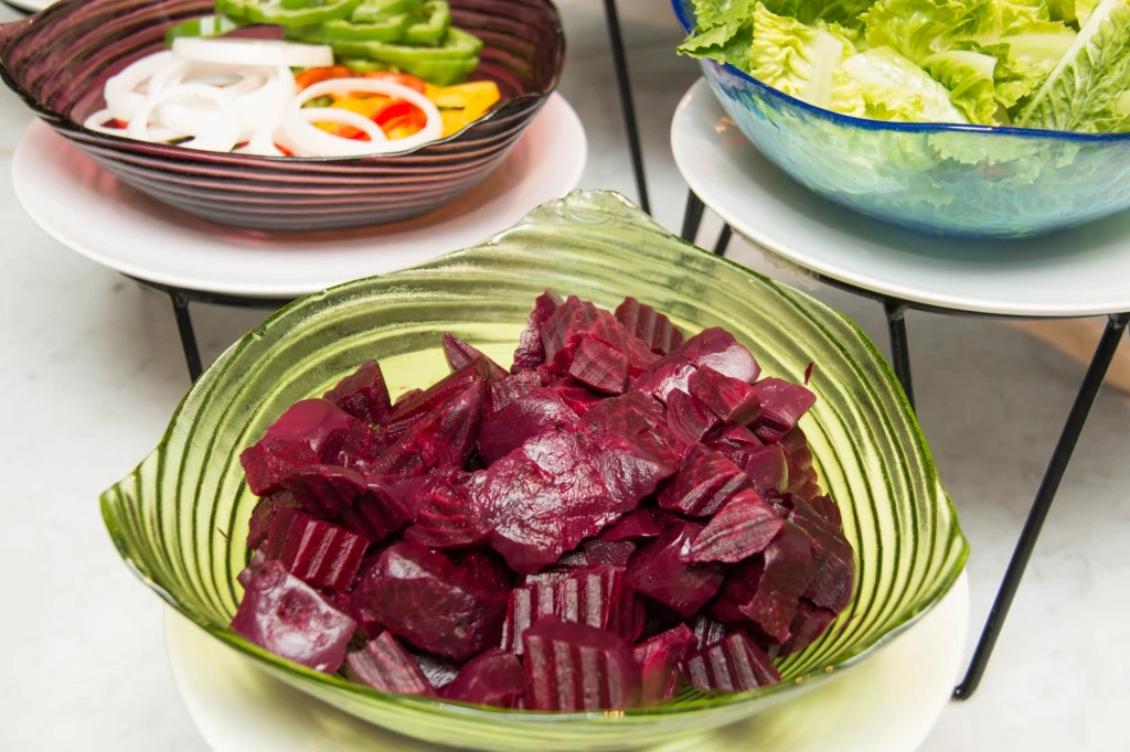 Kawałki buraków w zielonej misce na pierwszym planie, w tle pozostałe miski z pokrojonymi warzywami: plasterki cebuli, papryka, sałata.