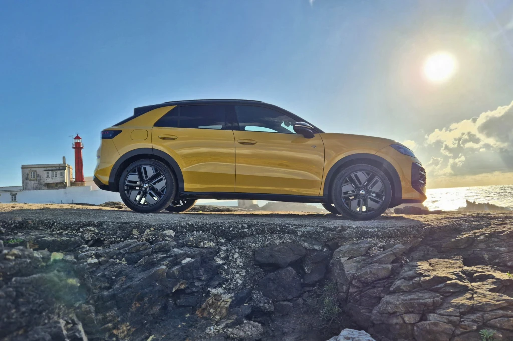 Nowy Volkswagen T-Roc zachował sylwetkę poprzednika, ale jest od niego o ponad 12 cm dłuższy Żółty nowoczesny SUV zaparkowany na tle urwiska, w pobliżu czerwono-białej latarni morskiej, przy słonecznej pogodzie z wyraźnie widocznym słońcem nisko nad horyzontem.