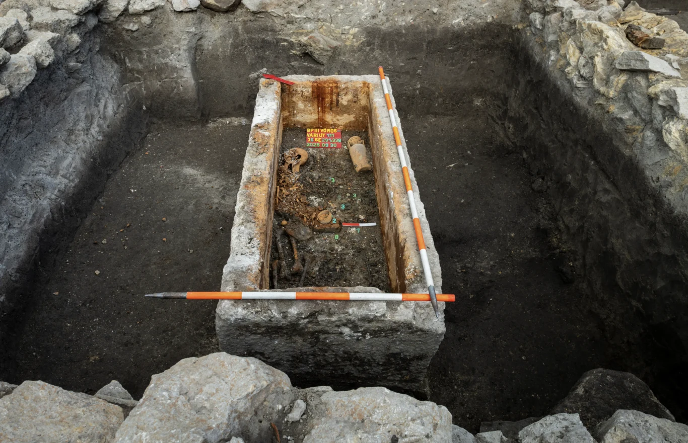 Archeolodzy z Muzeum Historycznego Budapesztu dokonali jednego z najważniejszych odkryć w historii węgierskiej archeologii Kamienna trumna z odkrytymi szczątkami ludzkimi i metalowymi przedmiotami, umieszczona w wykopanym na ten cel grobie, otoczona przez warstwy ziemi oraz kamienne ściany wykopu. Wewnątrz widoczne narzędzia pomiarowe archeologów.
