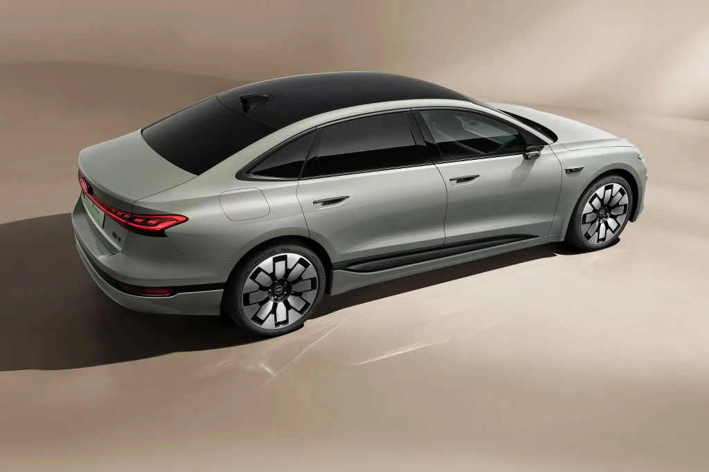 Nowoczesny srebrny samochód osobowy o dynamicznej sylwetce, z panoramicznym czarnym dachem i wyrazistymi felgami. Auto stoi na neutralnym tle, co podkreśla jego elegancki i aerodynamiczny design.