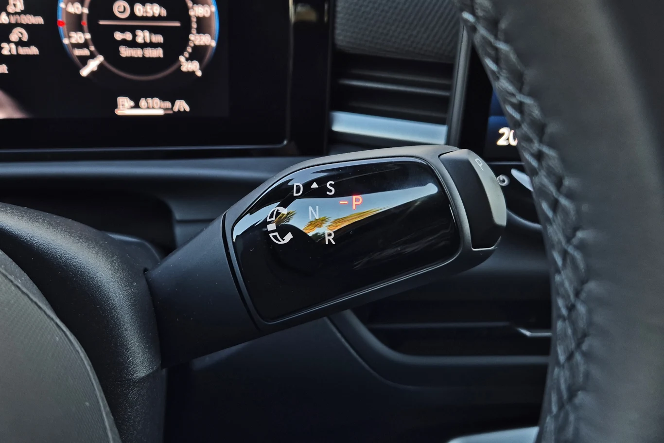 Tak jak w Tiguanie i Passacie - nowy T-Roc dostępny będzie tylko ze skrzynią automatyczną, której wybierak trafił na miejsce dźwigni wycieraczek Dźwignia zmiany biegów automatycznej skrzyni znajdująca się obok kierownicy, z widocznymi oznaczeniami trybów jazdy oraz fragment wyświetlacza z cyfrowymi wskaźnikami samochodu w tle.