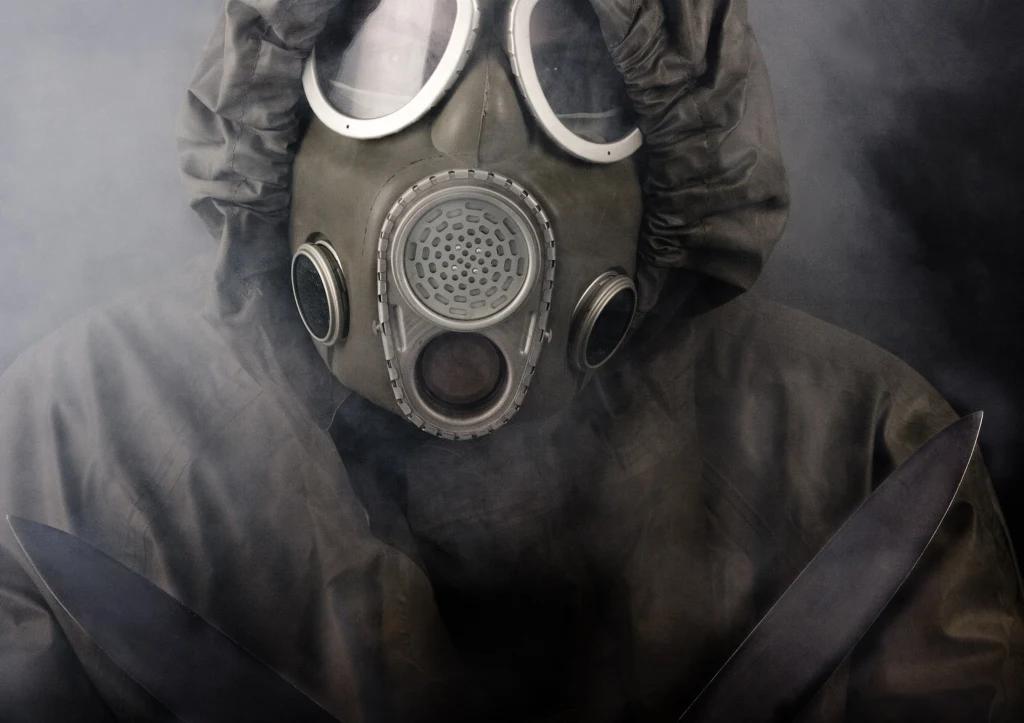Naukowcy ostrzegają: Niewiarygodny postęp w neuronauce ma mroczną stronę Osoba w kombinezonie ochronnym i masce gazowej, trzymająca dwa noże, otoczona przez gęsty dym.