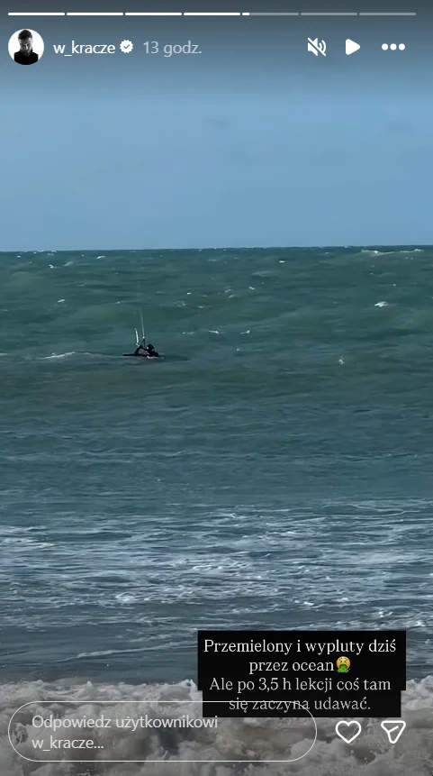 Osoba na desce surfingowej lub kitesurfingowej w oddali na wzburzonym oceanie, pochmurne niebo, w pierwszym planie fale rozbijające się o brzeg.