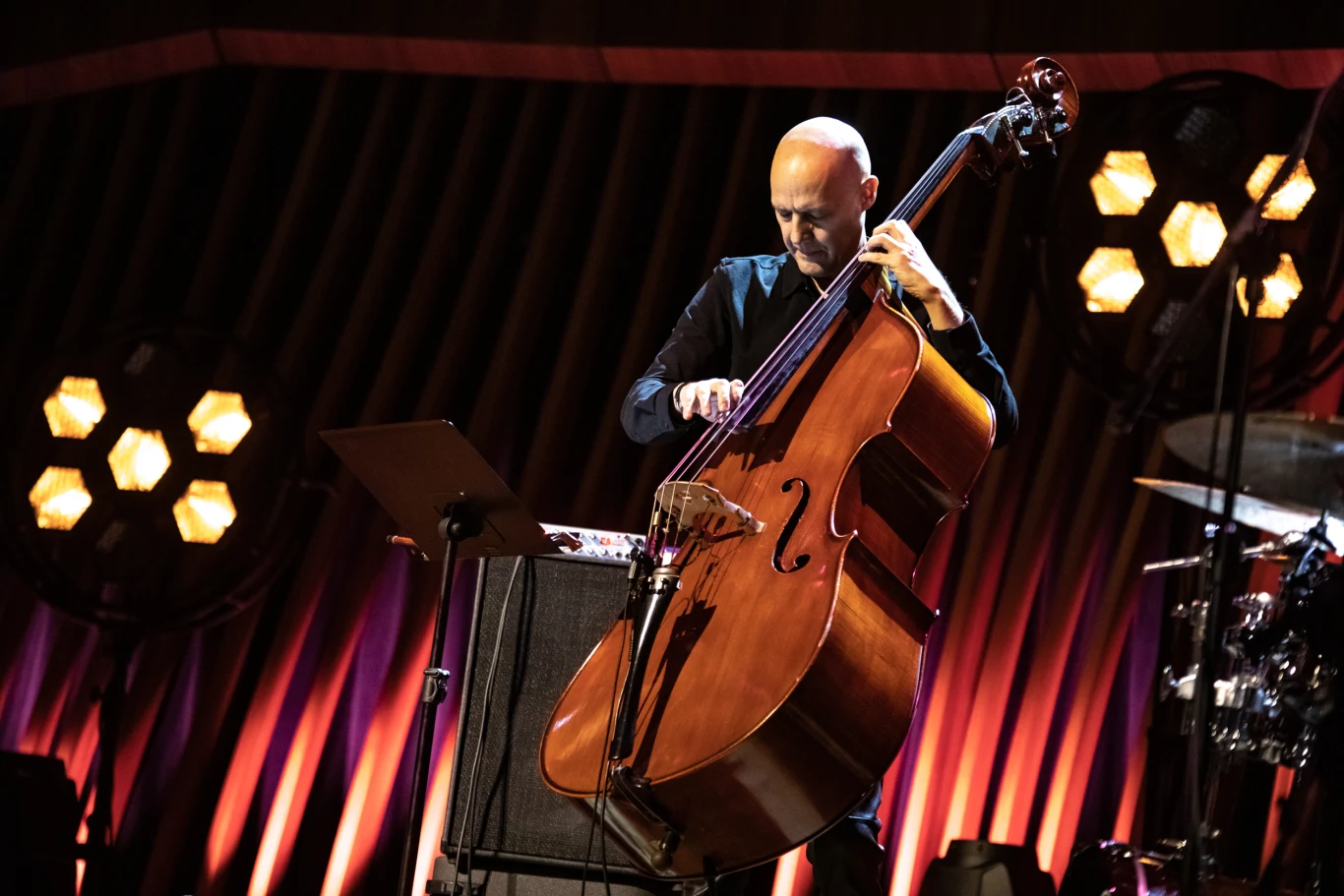 Muzyk grający na kontrabasie na scenie oświetlonej nastrojowym światłem, w tle dekoracje i pozostałe elementy zespołu.