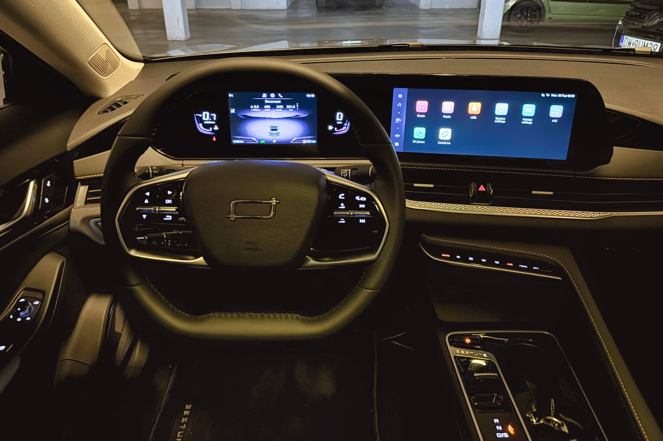 Wnętrze nowoczesnego samochodu z cyfrową deską rozdzielczą, dużym ekranem dotykowym po prawej stronie, kierownicą wielofunkcyjną oraz panelami sterowania przy fotelu kierowcy. Możliwość sterowania systemem multimedialnym oraz podstawowymi funkcjami poj...