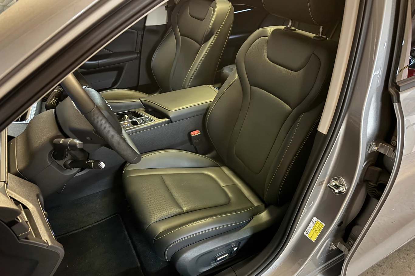 Nowoczesne, skórzane, czarne fotele w przedniej części pojazdu, kierownica z wielofunkcyjnymi przyciskami oraz konsola środkowa z podłokietnikiem i uchwytami na napoje.