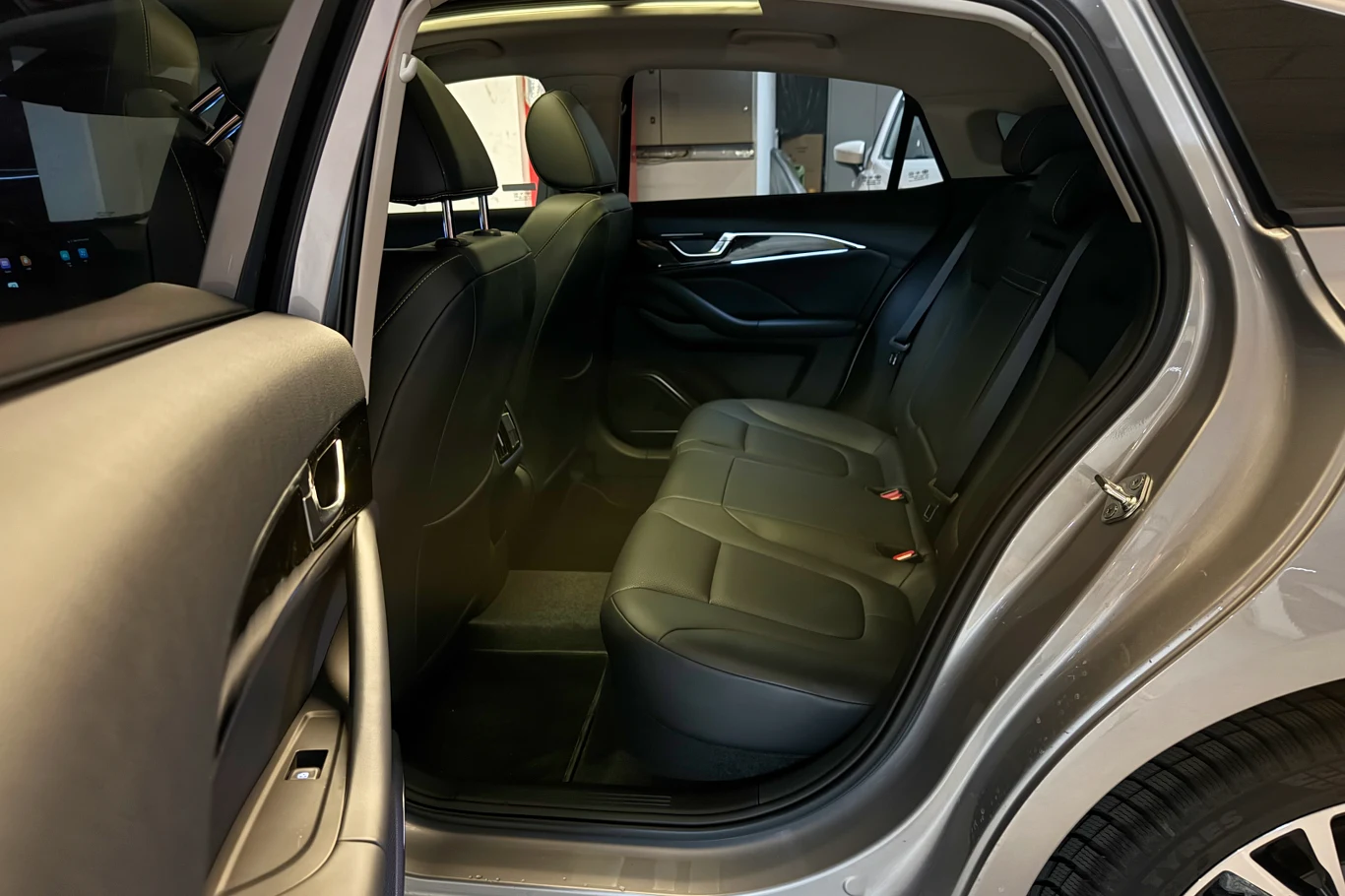 Wnętrze samochodu, widok na tylne siedzenia pokryte czarną tapicerką skórzaną, drzwi otwarte, wnętrze utrzymane w nowoczesnym stylu, widoczna przestrzeń dla pasażerów oraz podłokietnik.