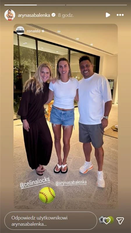 Trzy uśmiechnięte osoby stoją razem w jasnym wnętrzu, przy dużym przeszkleniu, dwie kobiety i mężczyzna. Kobieta po lewej ubrana w długą sukienkę, środkowa w białą koszulkę i krótkie dżinsowe szorty, mężczyzna w białej koszulce i szarych spodenkach. Na...