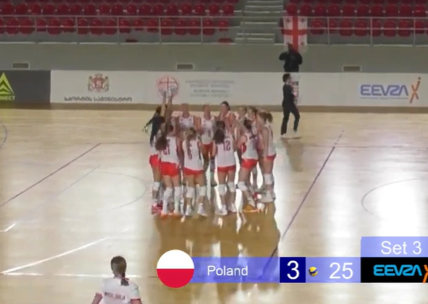 Polskie siatkarki zdobyły złoto Drużyna siatkarek ubrana w biało-czerwone stroje świętuje zwycięstwo na parkiecie hali sportowej, wokół zawodniczek pusty parkiet, w tle trybuny z niewielką liczbą kibiców oraz tablica wyników wskazująca zwycięstwo Polski w trzecim secie.