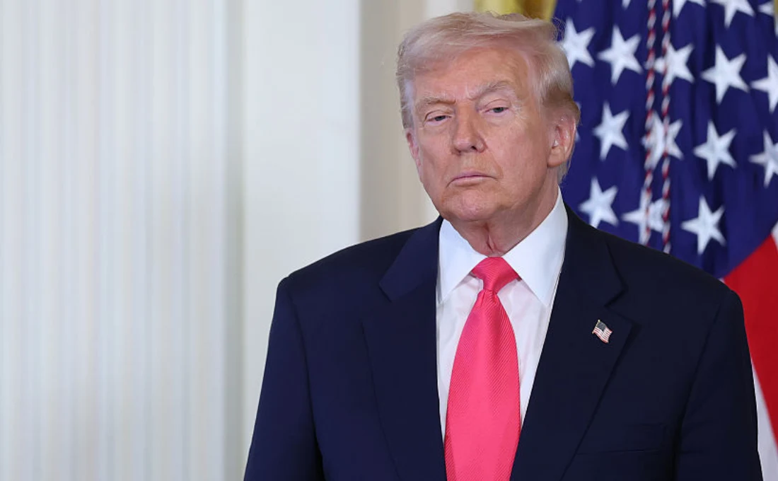 Donald Trump skrytykował władze Ukrainy i Unię Europejską Mężczyzna w garniturze i czerwonym krawacie stoi na tle flagi Stanów Zjednoczonych. Patrzy prosto w obiektyw z poważnym wyrazem twarzy.
