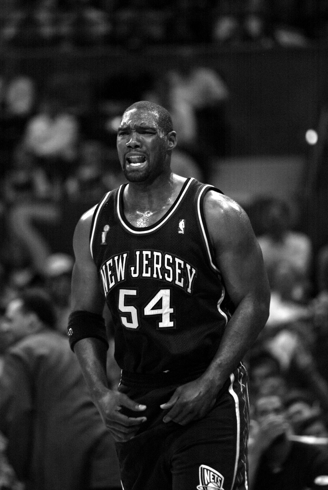 Rodney Rogers Koszykarz New Jersey Nets w trakcie emocjonującego momentu meczu, ubrany w czarny strój z numerem 54, wyraża silne emocje, w tle rozmyta publiczność.
