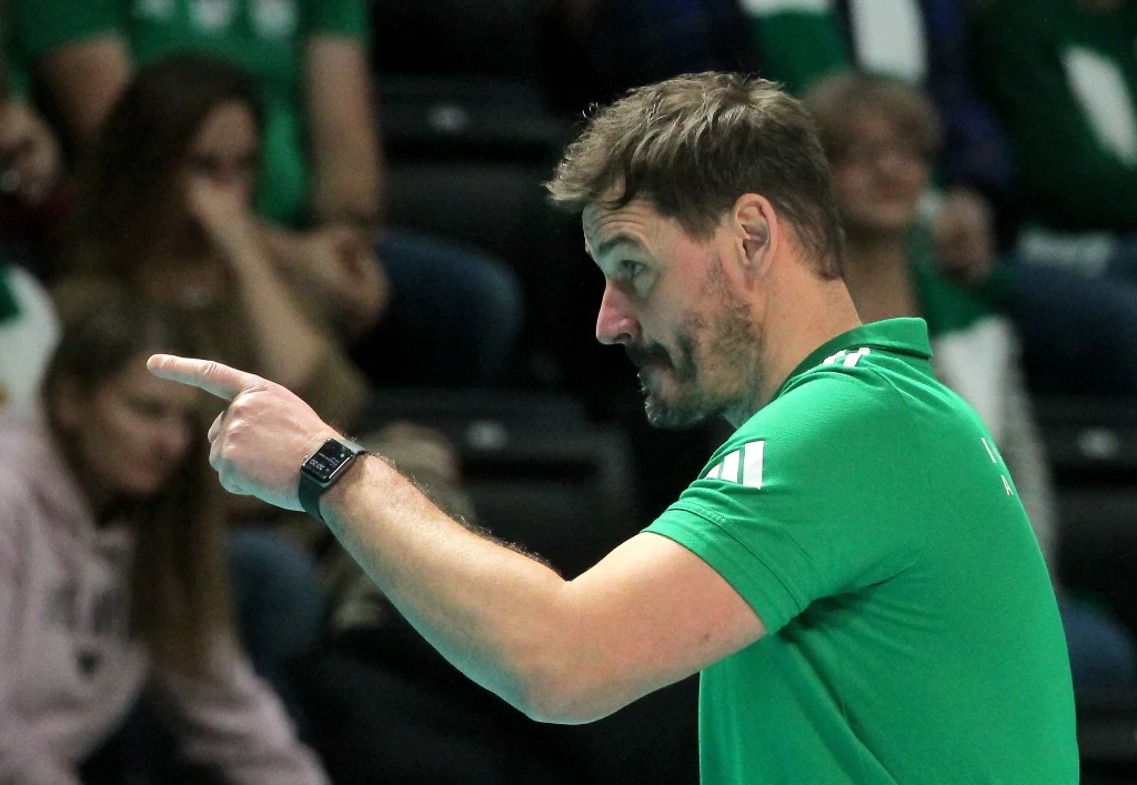 Daniel Pliński to legenda siatkarskiej reprezentacji Polski. W tym sezonie z powodzeniem prowadzi Indykpol AZS Olsztyn Mężczyzna w zielonej koszulce stojący na tle rozmytej publiczności wskazuje palcem, wyraźnie skoncentrowany na czymś poza kadrem.