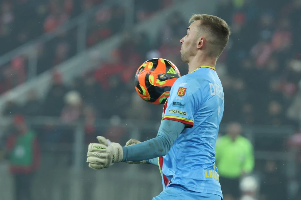 Bramkarz gości Xavier Dziekoński okazał się dla gospodarzy zbyt wymagającym rywalem Bramkarz ubrany w niebieski strój łapie piłkę podczas meczu piłki nożnej, na trybunach widać rozmytą publiczność.