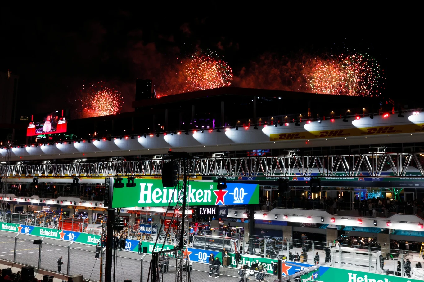 Tor wyścigowy oświetlony w nocy, nad trybunami widowiskowy pokaz fajerwerków. Po bokach dominują reklamy sponsorów, w tym Heineken. W tle kibice obserwują wydarzenie sportowe.