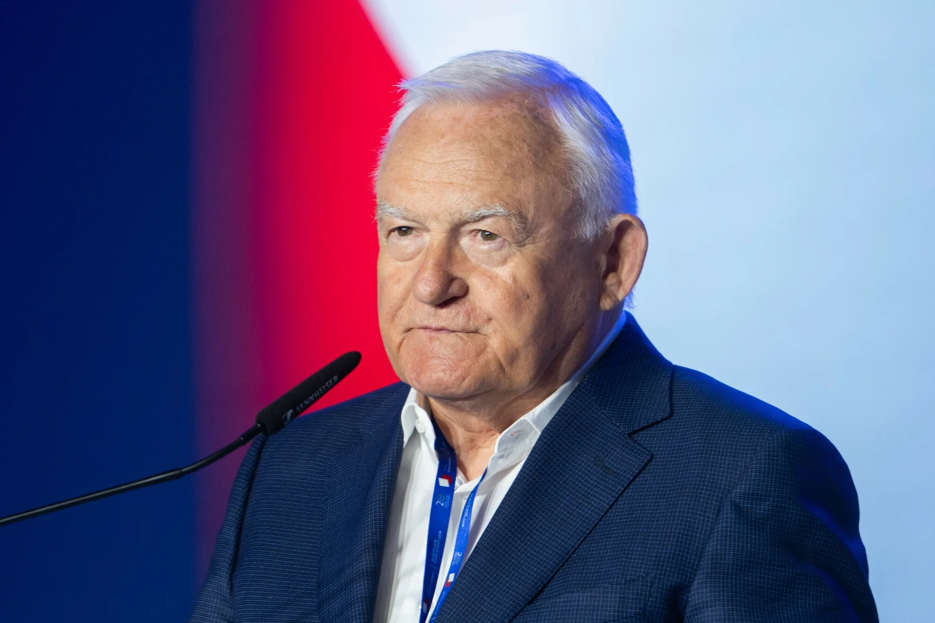 Były premier Leszek Miller zmienił zdanie o prezydencie Karolu Nawrockim Starszy mężczyzna w garniturze stoi przy mikrofonie na tle biało-czerwonego tła nawiązującego do flagi; skupiony wyraz twarzy sugeruje udział w oficjalnym wydarzeniu lub przemówieniu.