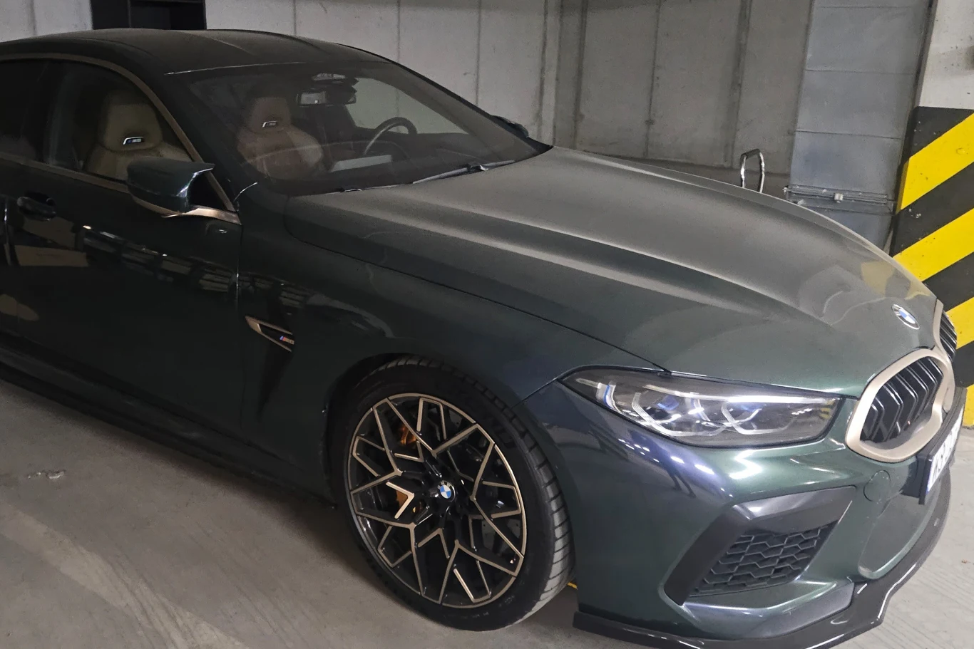 Luksusowy samochód BMW w ciemnozielonym kolorze stoi na parkingu podziemnym, wyróżnia się sportową sylwetką, charakterystycznym przodem z dużymi wlotami powietrza, stylowymi felgami oraz widocznymi odznakami modelu M.