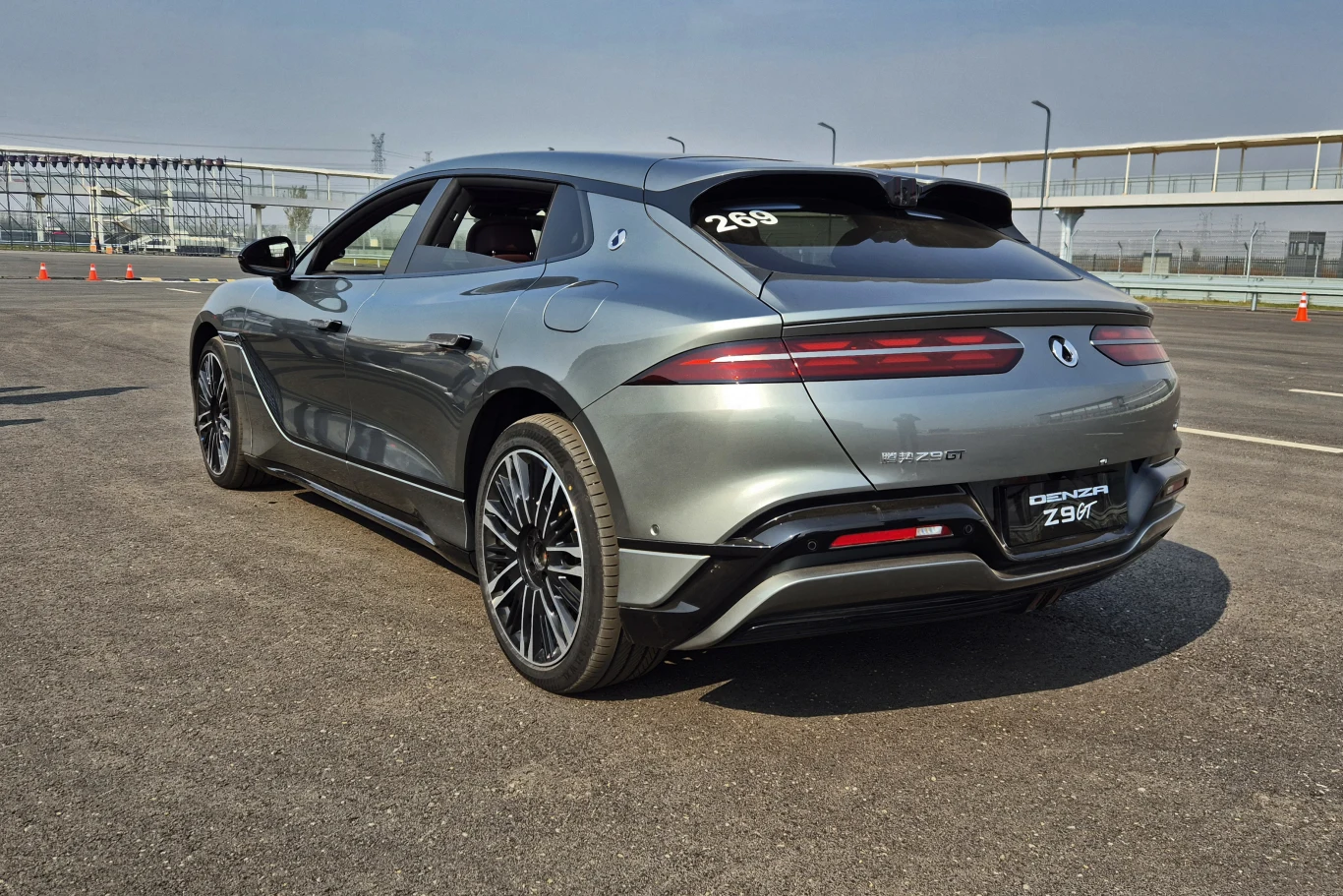 Nowoczesny, sportowy samochód elektryczny w kolorze szarym na torze testowym, z szerokimi felgami, przyciemnianymi szybami i charakterystycznymi, poziomymi światłami tylnymi.