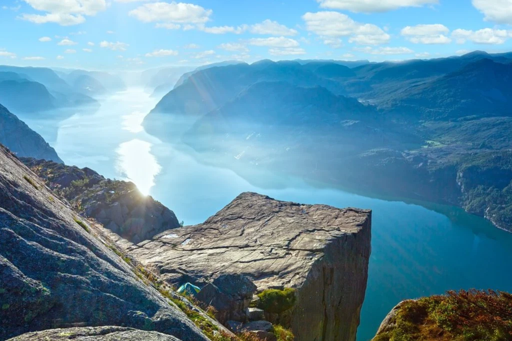 PLL LOT właśnie wystartował z bezpośrednimi połączeniami z Warszawy do Stavanger. Malowniczy płaskowyż Preikestolen wznoszący się nad głębokim, błękitnym fiordem, otoczony górzystym krajobrazem pod błękitnym niebem z rozproszonymi chmurami. Odbicie słońca na powierzchni wody tworzy efektowny świetlisty pas.