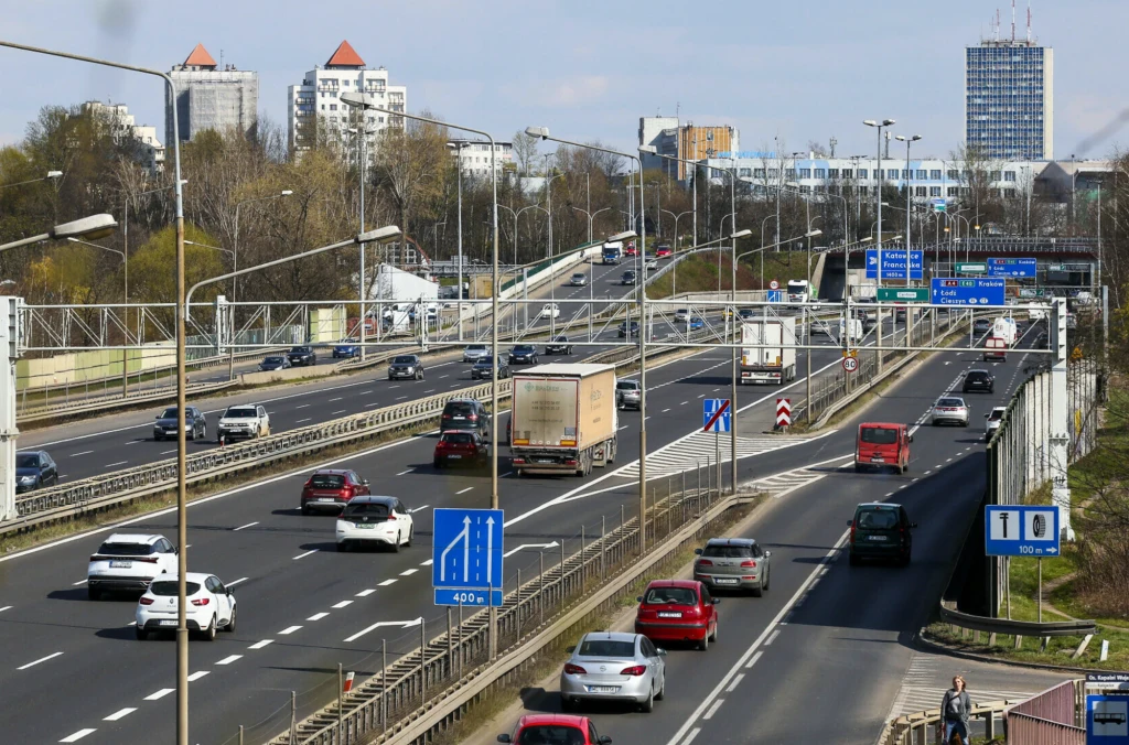 Katowice chcą zadaszyć A4. Powstanie unikalna konstrukcja nad autostradą. Ruchliwa miejska arteria z kilkupasmową jezdnią, pojazdami osobowymi i ciężarowymi, sygnalizacją drogową oraz wysokimi budynkami w tle, widoczne znaki drogowe i separacja pasów ruchu.