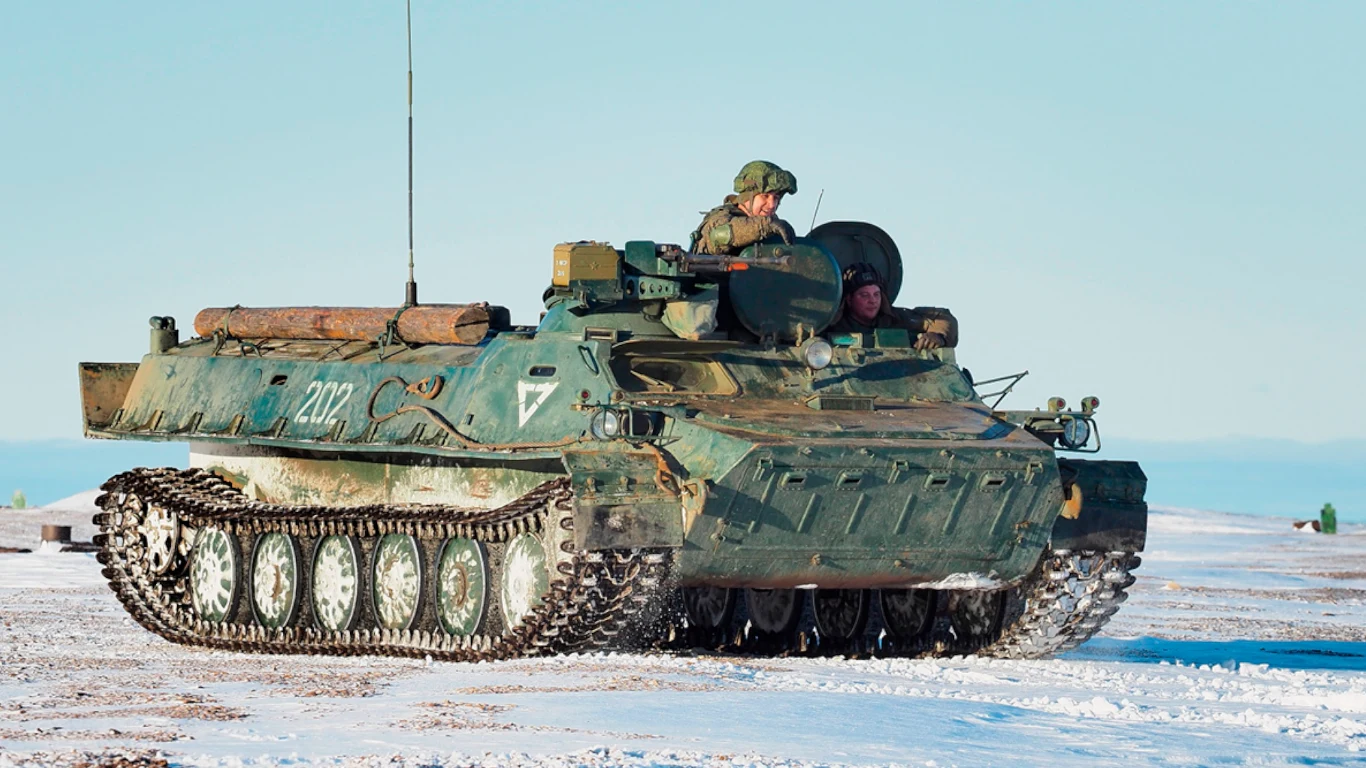 Opancerzony pojazd wojskowy poruszający się po ośnieżonym terenie, widocznych kilku żołnierzy w mundurach oraz charakterystyczne oznaczenia na boku pojazdu.