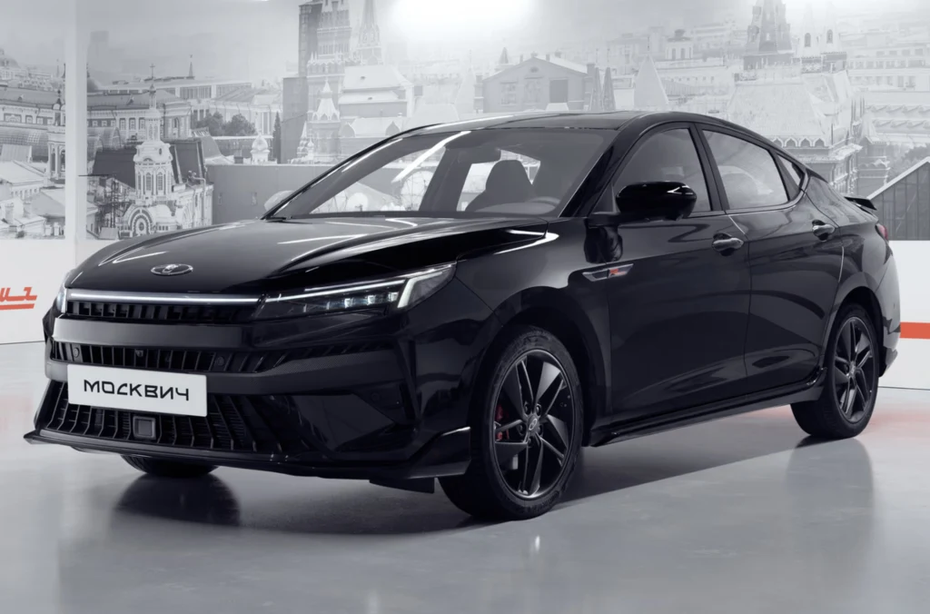 Pierwsza partia Moskwiczów 6 dotarła już na wyspę, ale pojawiły się wątpliwości dotyczące ich realnego przeznaczenia i możliwości użytkowania. Czarny, nowoczesny samochód osobowy marki Moskwicz ustawiony w jasnym, eleganckim wnętrzu na tle czarno-białych grafik przedstawiających zabudowę miejską.