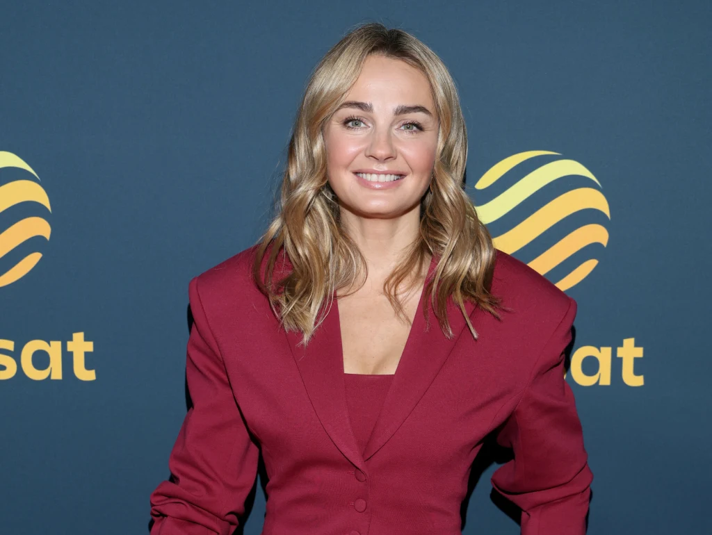 Małgorzata chętnie bawi się modą Blondynka w eleganckiej bordowej marynarce, uśmiechnięta, stoi na tle ściany z logo Polsatu.