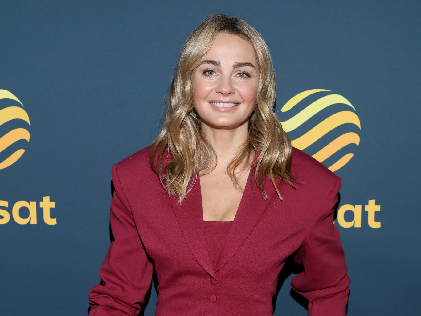 Małgorzata chętnie bawi się modą Blondynka w eleganckiej bordowej marynarce, uśmiechnięta, stoi na tle ściany z logo Polsatu.