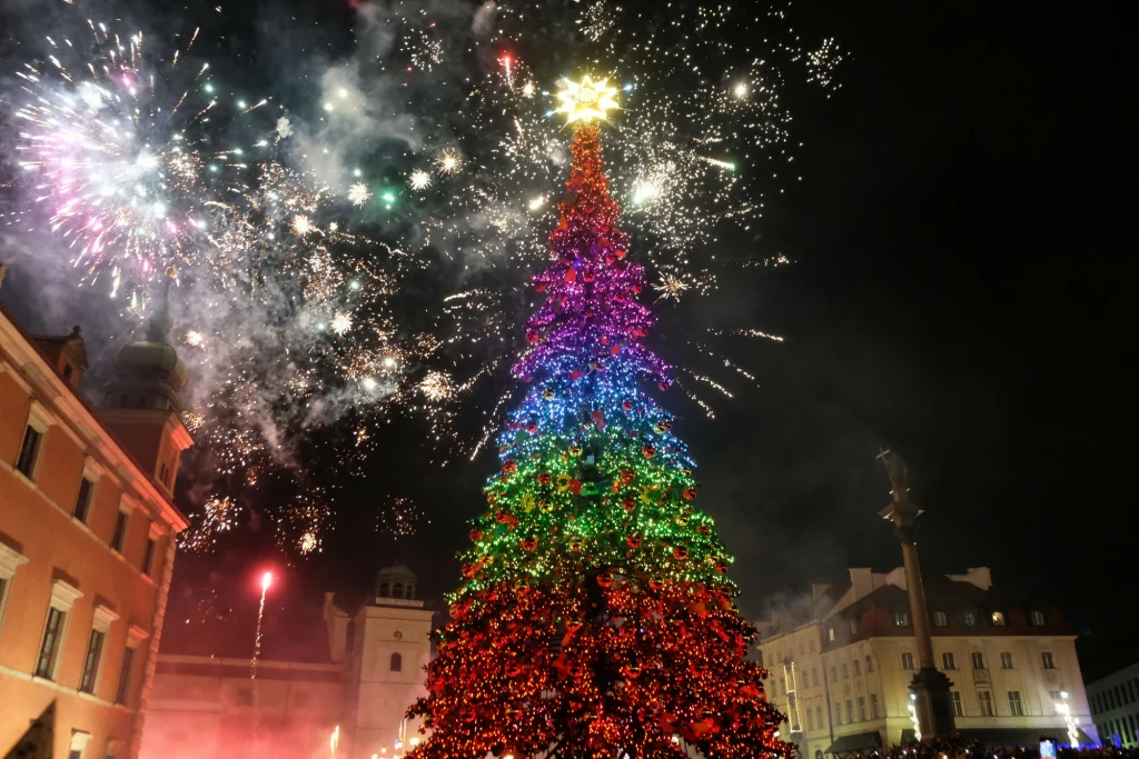 W 2026 roku nie tylko Wigilia, ale rónież Sylwester może być dniem wolnym od pracy Kolorowo oświetlona choinka ustawiona na placu otoczonym zabytkowymi budynkami, nad którą rozbłyskają fajerwerki na nocnym niebie.