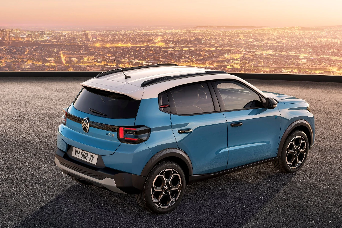 Niebieski samochód Citroën C3 Aircross na tle panoramy miasta o zmroku, auto stoi na otwartej powierzchni z widocznym tyłem oraz częścią boczną, widoczne nowoczesne detale dizajnu.